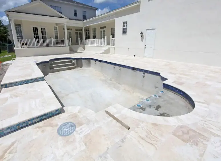 Large house with a swimming pool in the middle of it, surrounded by a travertine pool deck