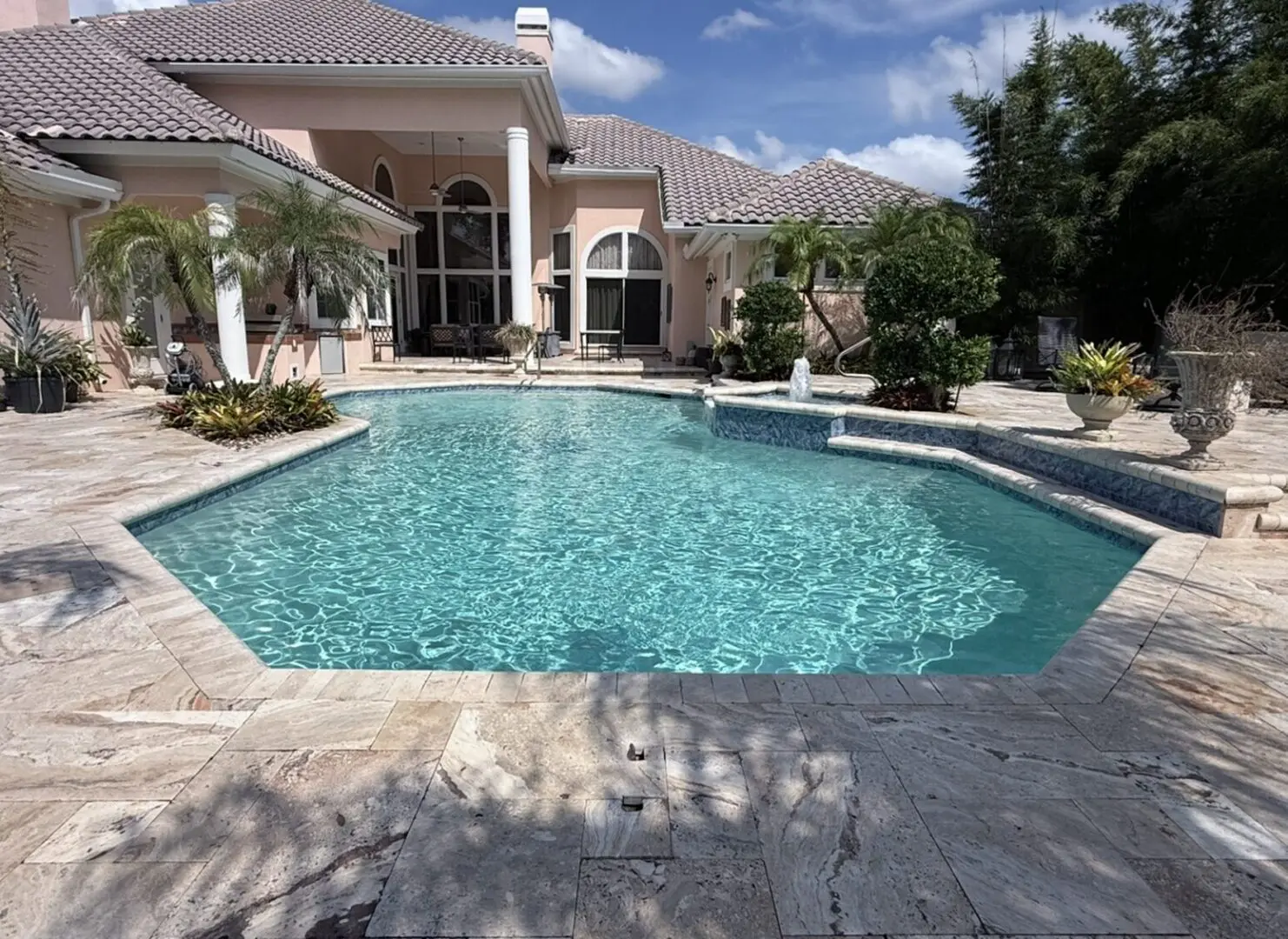 Large house with a swimming pool in front of it, surrounded by lush plants and trees