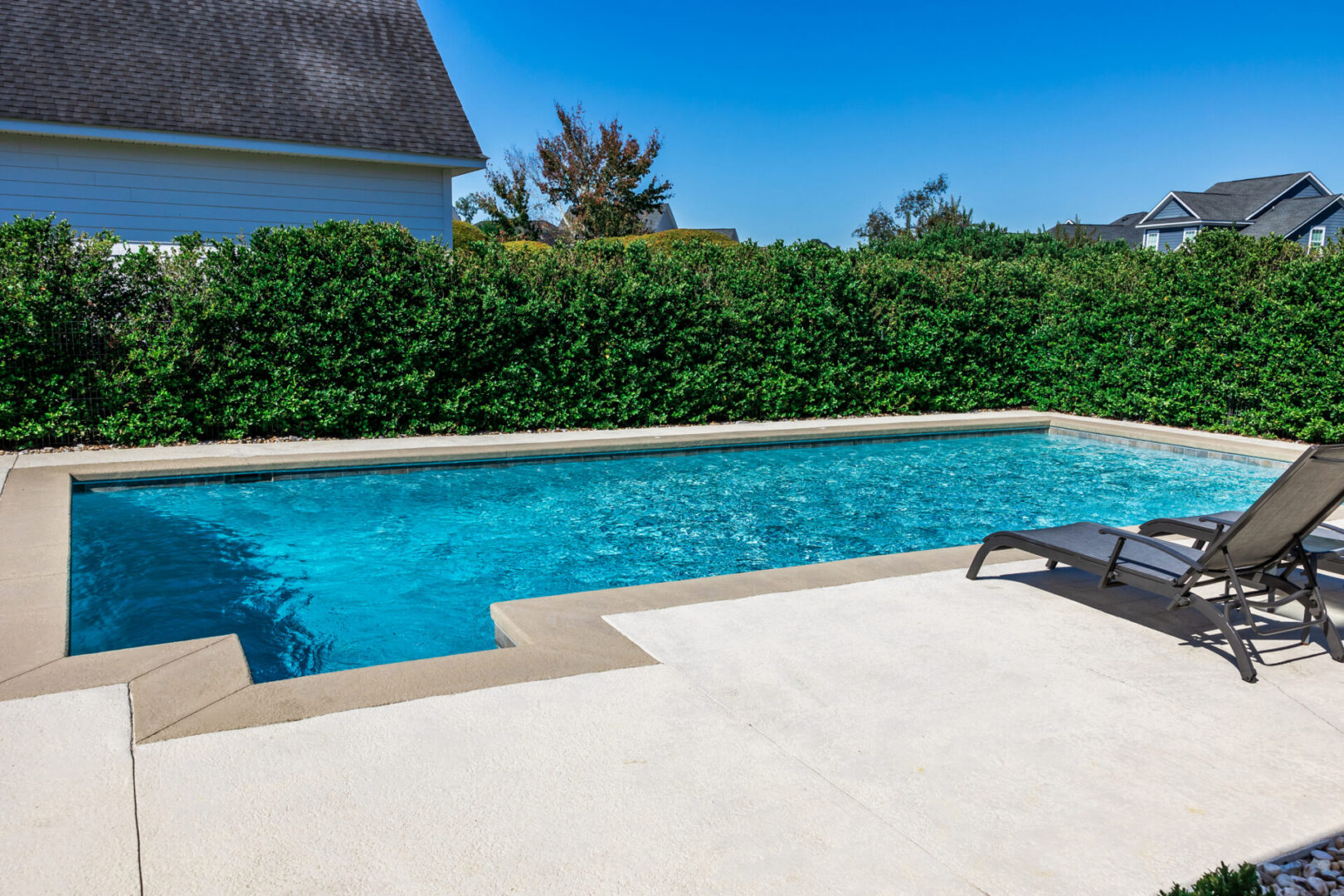 Swimming pool with a lounge chair in the middle of it surrounded by lush green bushes and trees
