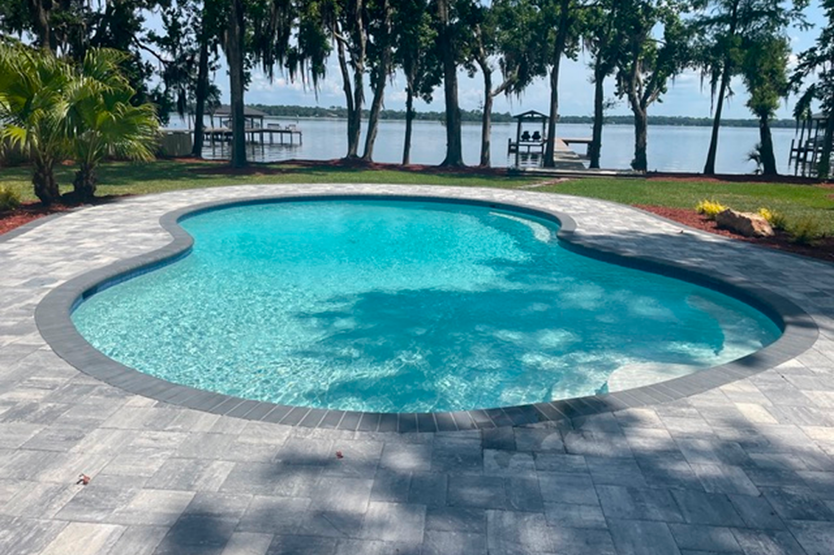 Swimming pool surrounded by lush green grass and trees, with a dock in the background