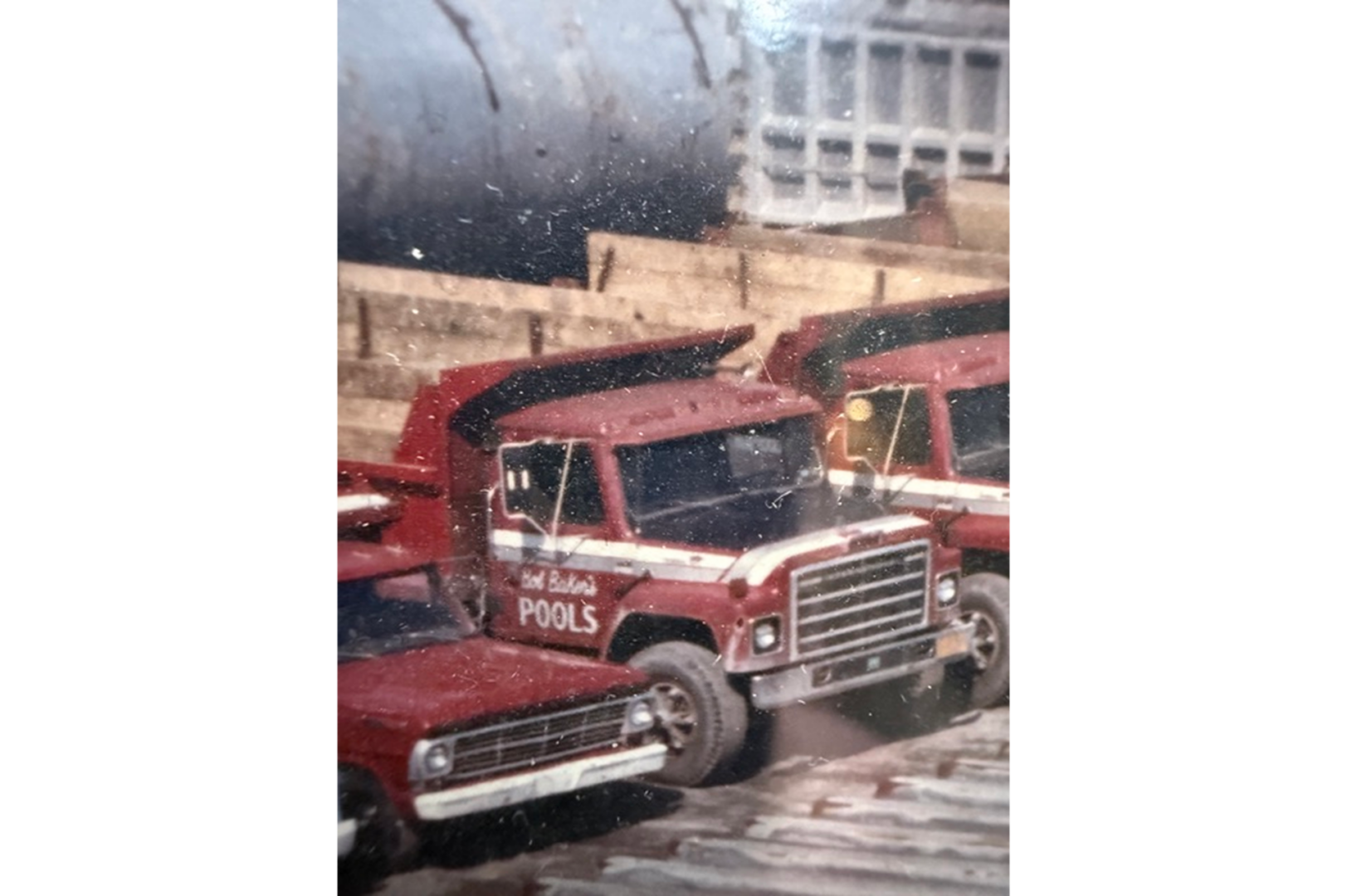 Two red trucks parked next to each other in front of a building, with a wall