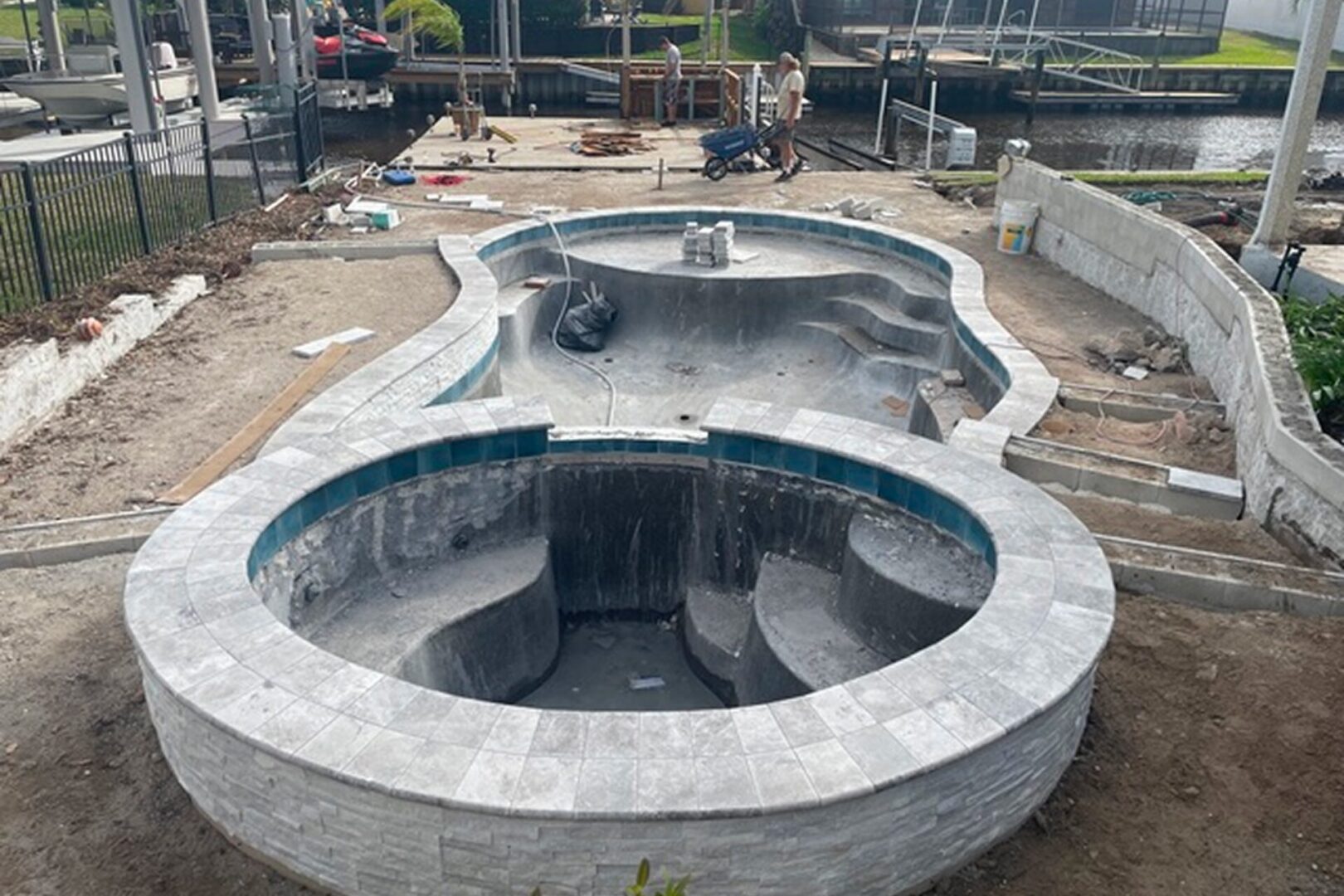 Concrete pool with a fire pit in the middle of it surrounded by a fence