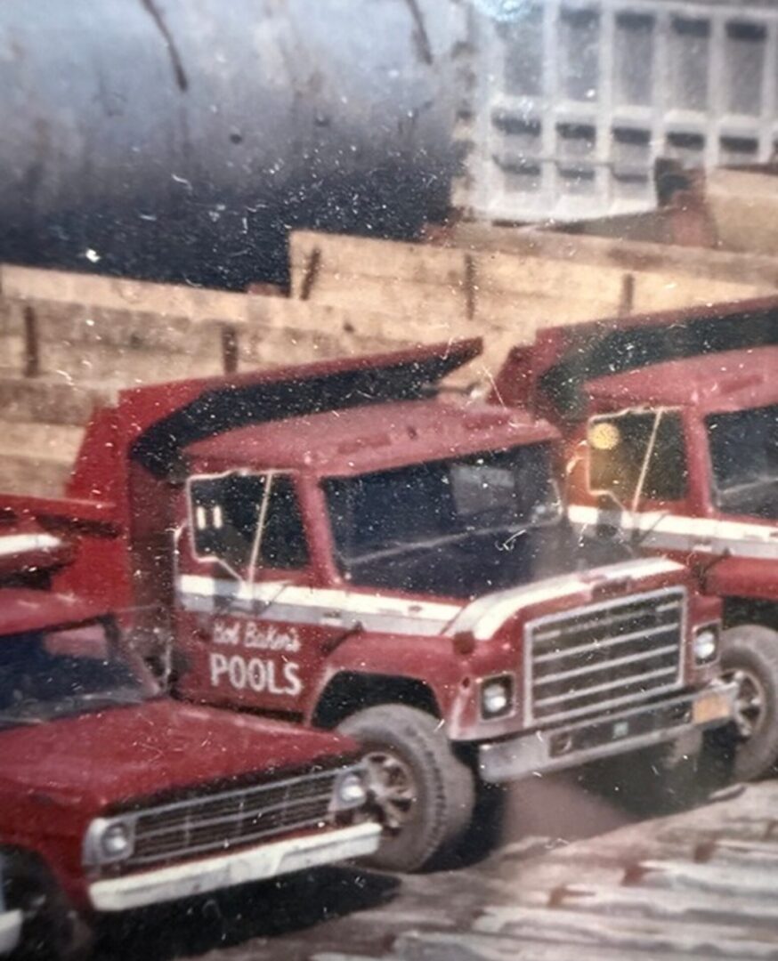 Two red trucks parked next to each other in front of a building, with a wall in the background