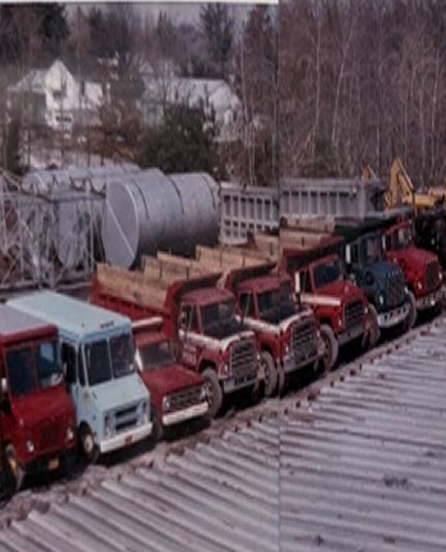 Group of trucks parked next to each other on top of a metal roof, with a crane in the background